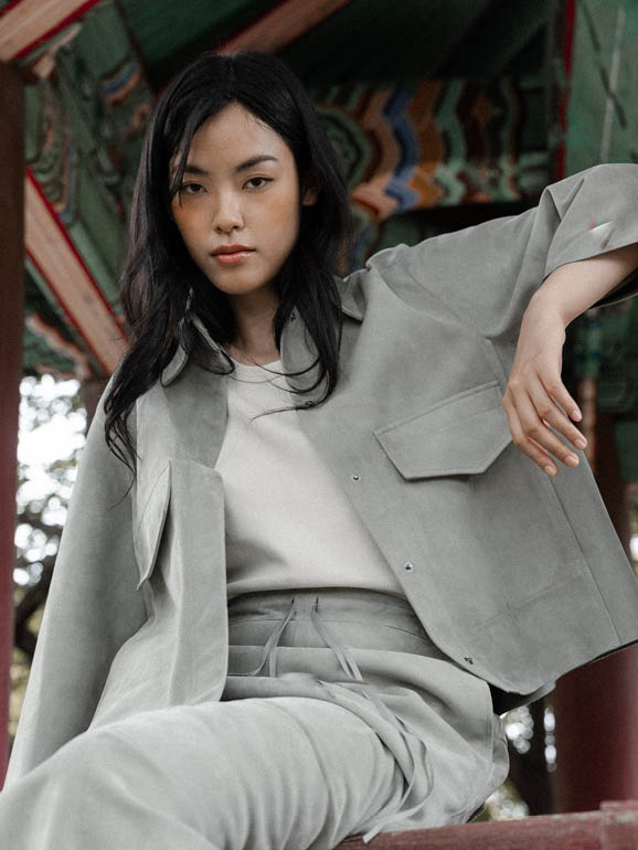 AYASSE Hemdjacke aus Veloursleder in Farbe Haze, modernes Design mit Taschen und Kragen, getragen im architektonischen Setting der Frühjahr Sommer 2026 Kollektion.