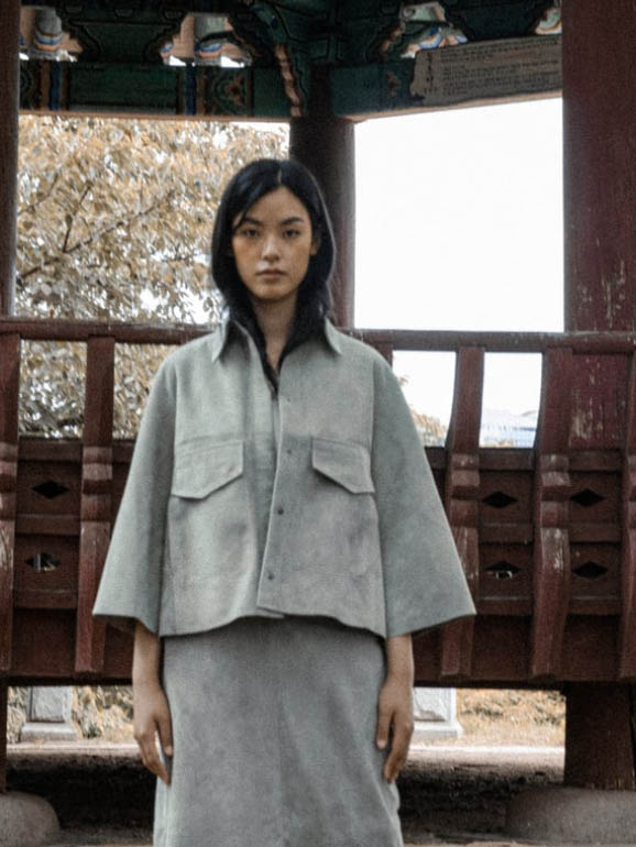 AYASSE Hemdjacke aus Veloursleder in Farbe Haze, modernes Design mit Taschen und Kragen, getragen im architektonischen Setting der Frühjahr Sommer 2026 Kollektion.